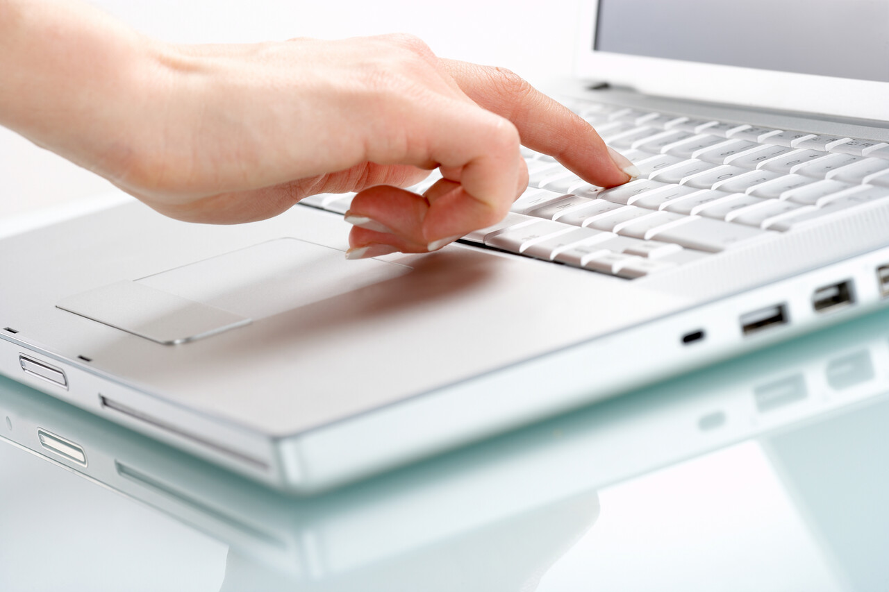One press of a finger...Modern laptop isolated on white with reflections on glass table.